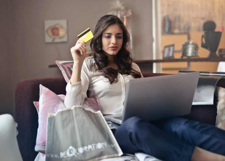Woman holding yellow credit card in front of her laptop