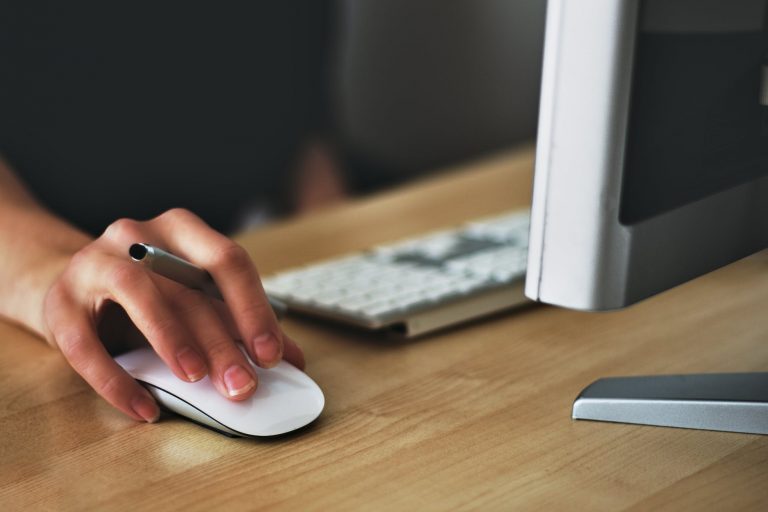 Person clicks on white mouse on a wooden table