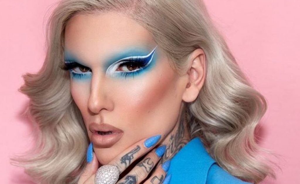 Beauty content creator Jeffree Star make up artist blue eyeshadow blue nails blue jacket pink background