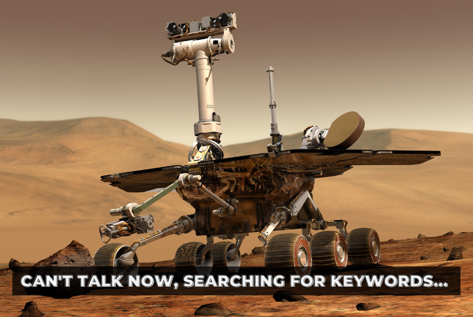 A robot on wheels drives through the desert. Text overlaid: "Can't talk now, searching for keywords"