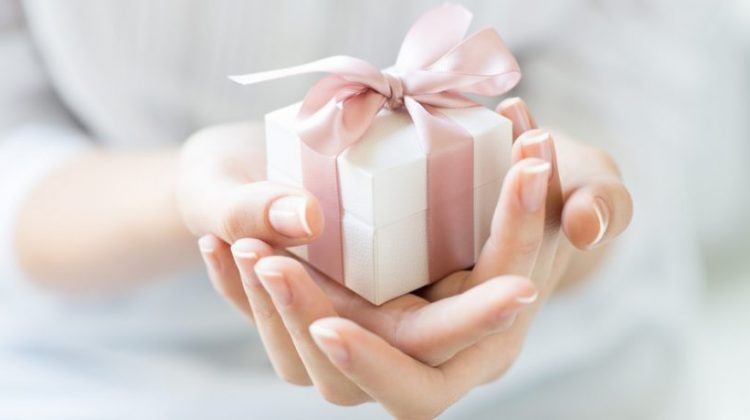 Woman's hands holding a small gift with a pink bow.