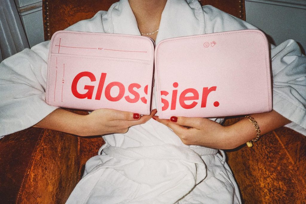 Glossier beauty bags in pin held by a woman in a bathrobe.