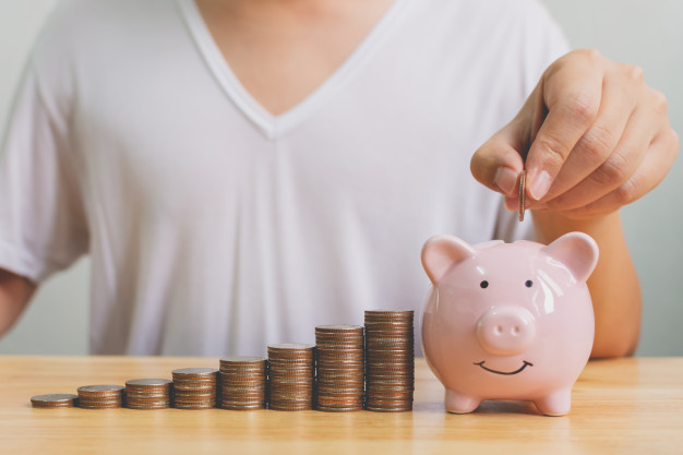 Person putting one of the coins from the stack into a piggy bank.