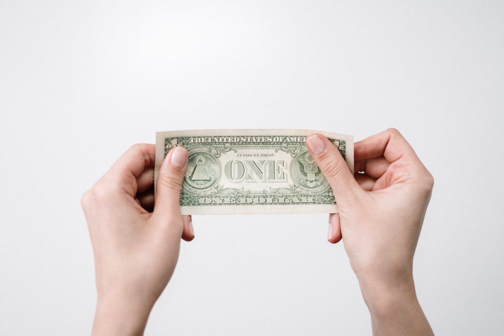 One dollar bill being held in both hands, representing the cost of acquiring customers for businesses. 